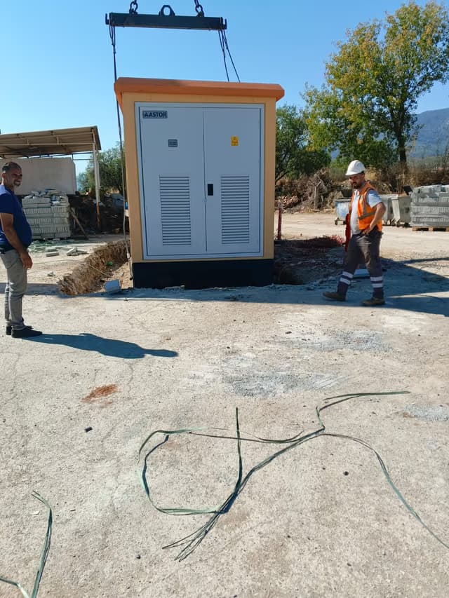 Beton köşkün vinçle temeline indirilmesi; iki teknisyen yerleşimi yönlendiriyor