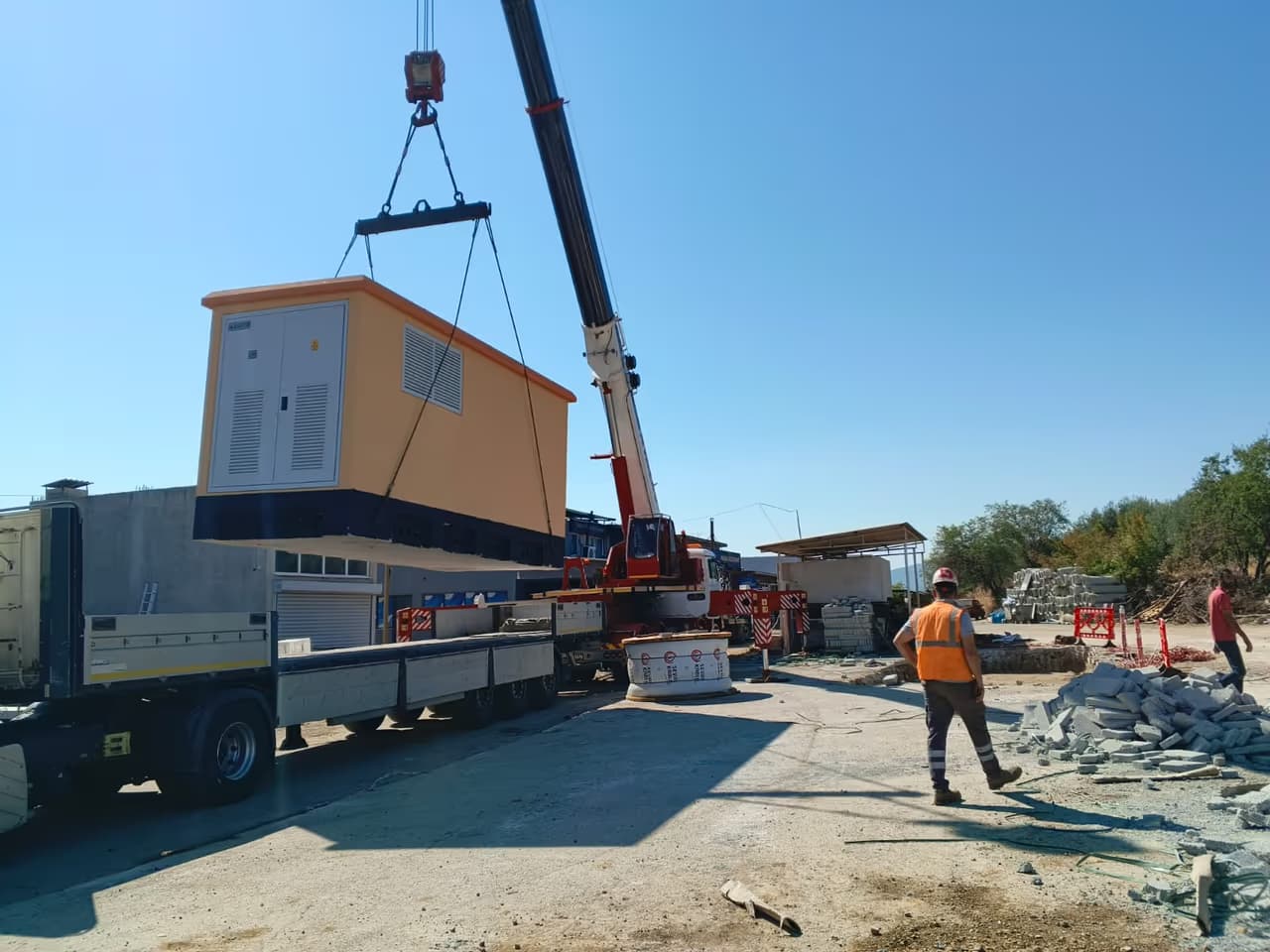 Beton köşk kamyondan vinçle alınıyor; saha ekibi çevrede güvenlik alıyor